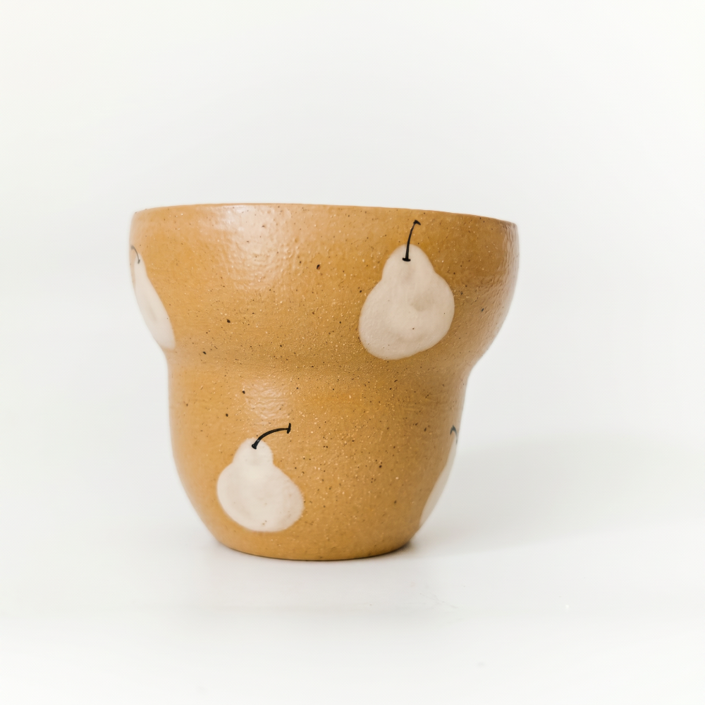 A clean, eye-level studio shot of a stepped ceramic cup by Kove Ceramics against a white background, highlighting its warm glossy mustard yellow glaze, rustic clay speckles, and hand-painted pear motifs.
