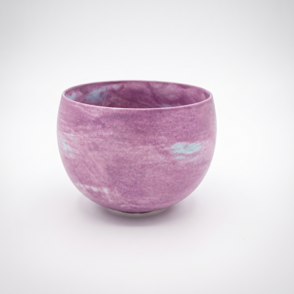 A slightly elevated studio shot of a round, handleless ceramic tumbler by Kove Ceramics, revealing its delicate rim and the seamless flow of its lilac and white watercolor matte glaze on a clean background.