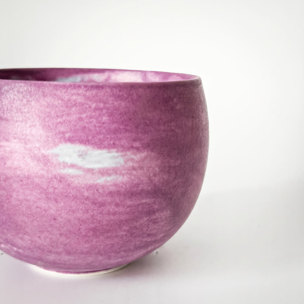 An extreme macro close-up of a round ceramic matcha cup by Kove Ceramics, highlighting the tactile matte surface texture and the dreamy, swirling brushstrokes of its purple and white watercolor glaze.