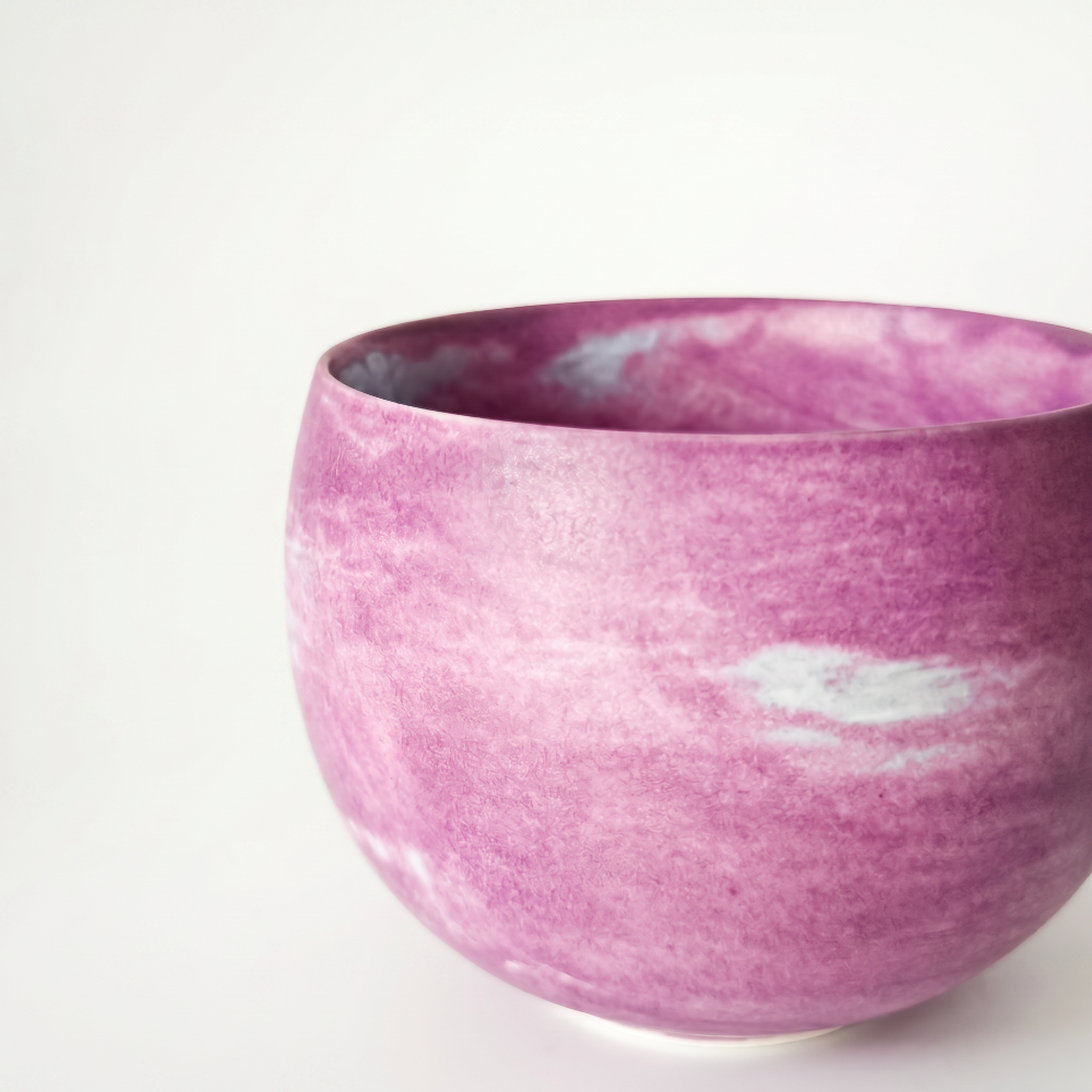 An off-center macro close-up of a handmade ceramic matcha cup by Kove Ceramics, focusing on the delicate rim and the textured, matte orchid pink and white marbled glaze against a soft white background.
