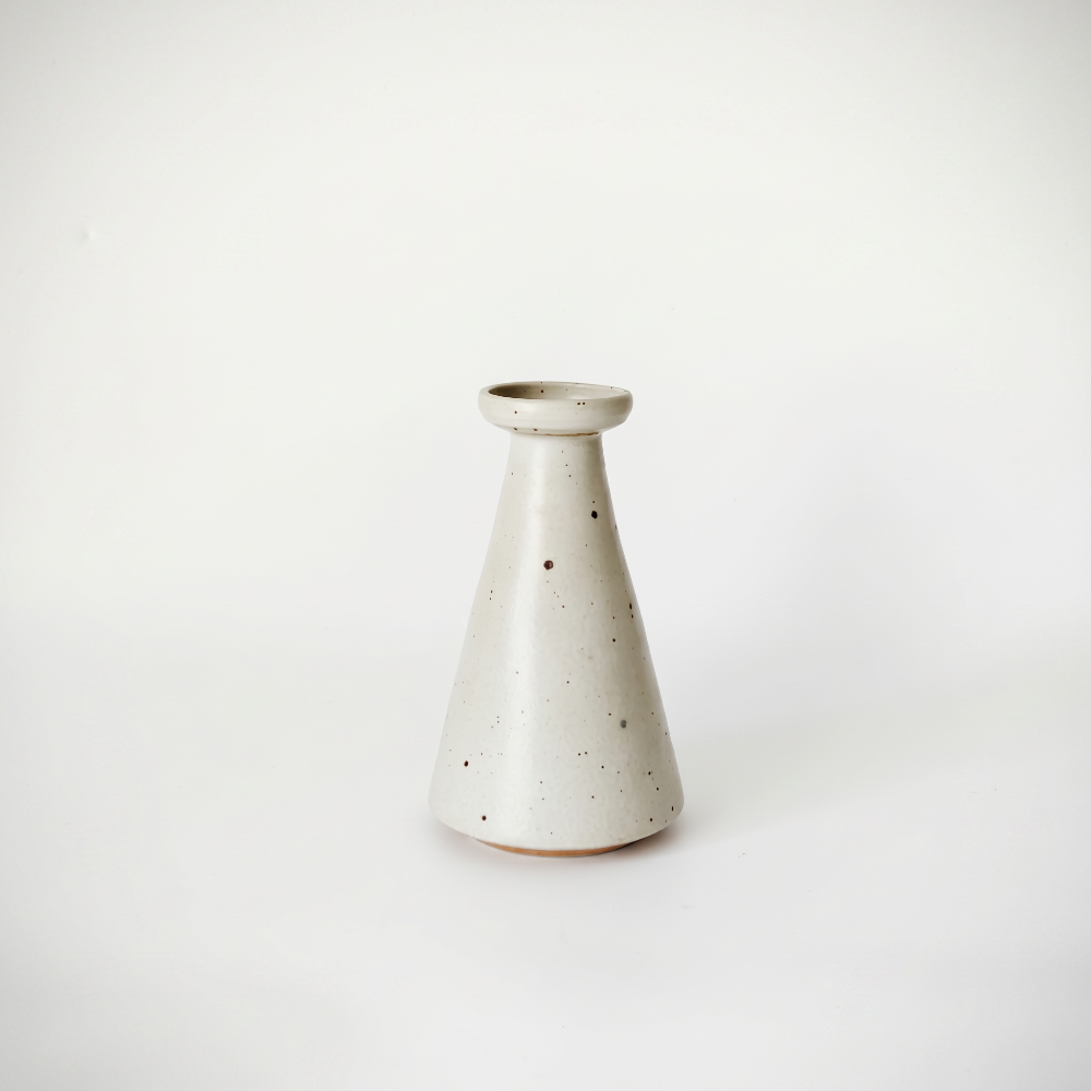 A modern minimalist ceramic bud vase crafted by Kove Ceramics, featuring a clean conical silhouette and a smooth cream glaze with natural dark speckles