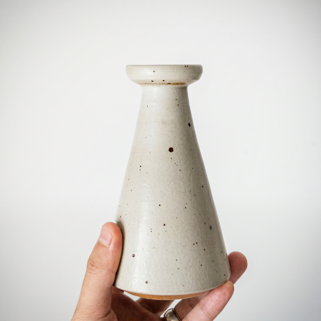 A hand holding a speckled cream conical ceramic bud vase by Kove Ceramics, demonstrating the actual size, scale, and beautiful tactile glaze of the handmade pottery piece