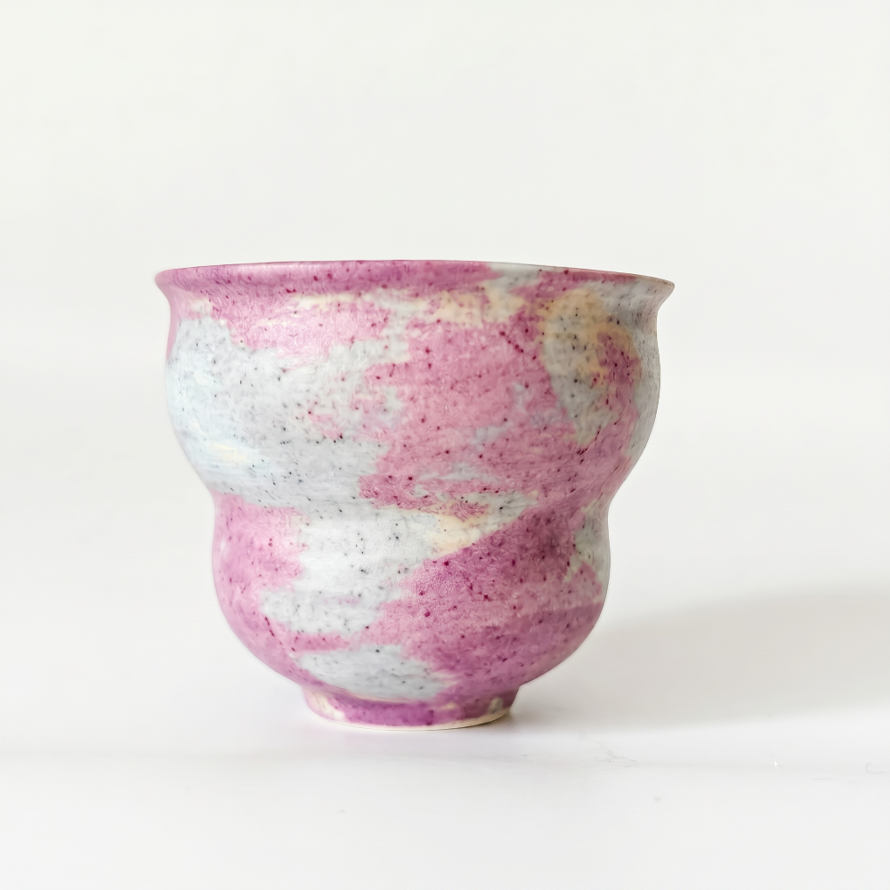 A clean studio shot of a handleless, stepped ceramic cup by Kove Ceramics on a white background. The unique piece features a gently flared rim, a tapered waist, and a dreamy pink and white marbled watercolor glaze applied over rustic, speckled clay.