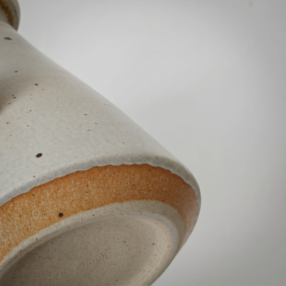 An extreme close-up of the ceramic vase underside by Kove Ceramics, revealing a rustic exposed clay band, a speckled glaze finish, and authentic concentric wheel-thrown rings on the base